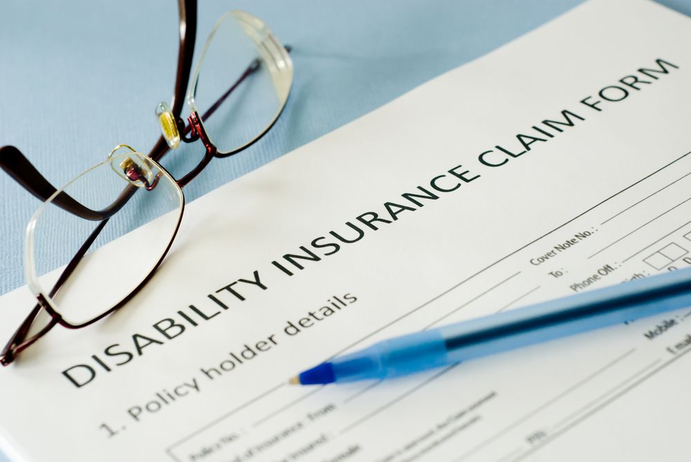 Disability insurance paperwork, eyeglasses, and pen on a desk.